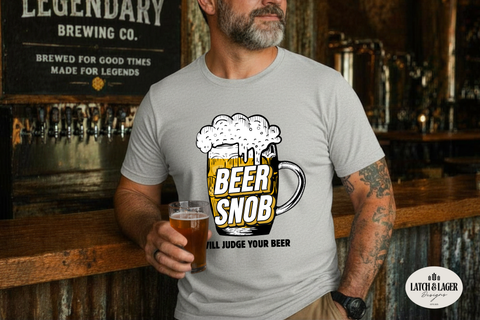 Man wearing a 'Beer Snob' t-shirt holding a beer in a bar setting.
