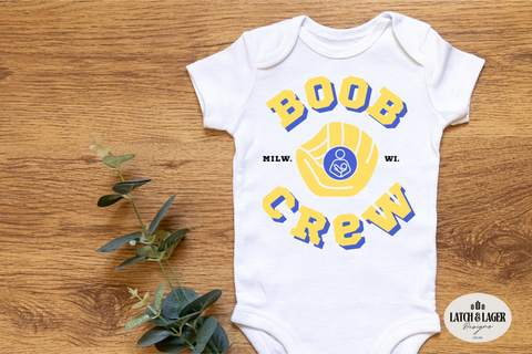 White baby onesie with 'BOOB CREW' text and graphic on a wooden surface