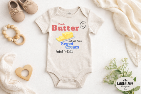 Baby onesie with vintage-style dairy advertisement design on a white surface with toys and a blanket.
