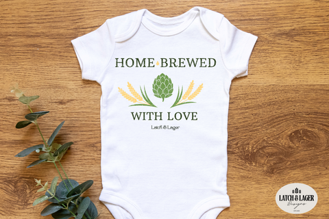 White baby onesie with 'Home Brewed with Love' text on a wooden surface