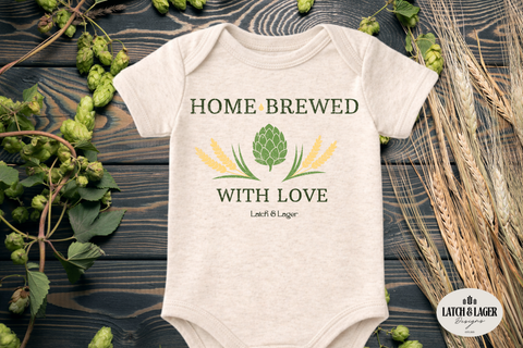 Baby onesie with 'Home Brewed with Love' design on a wooden surface with hops and barley.