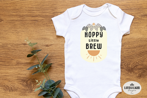 White baby onesie with 'Hoppy Little Brew' design on a wooden surface