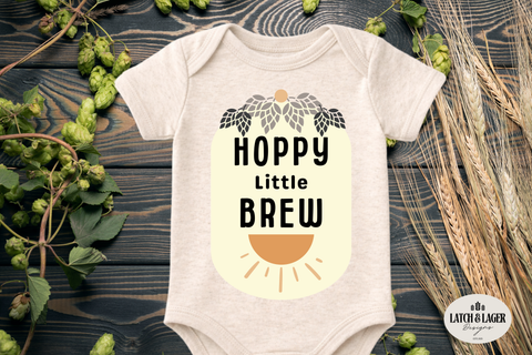 Baby onesie with 'Hoppy Little Brew' design on a wooden surface with hops and barley.