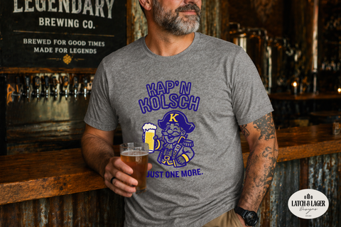 Man wearing a 'Kap'n Kolsch' t-shirt holding a beer in a bar setting.