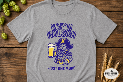 Gray t-shirt with 'Map'n Holsch Just One More' design on a wooden surface with hops and wheat.
