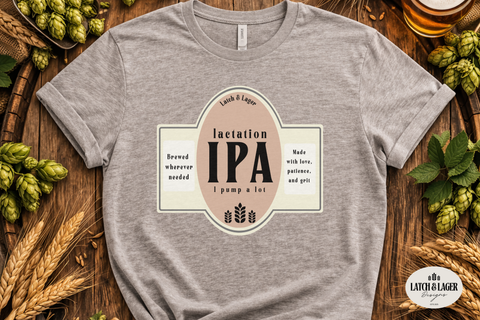 Gray t-shirt with 'Lactation IPA' design on a wooden surface with hops and beer.