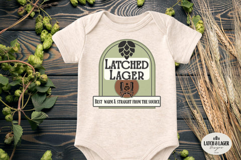 Baby onesie with 'Latched Lager' design on a wooden surface with hops and wheat.