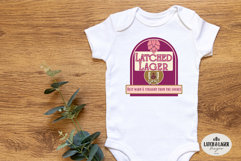 White baby onesie with 'Latched Lager' design on a wooden surface