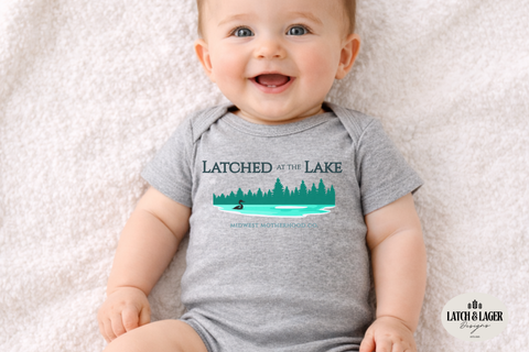 Baby wearing a gray onesie with 'Latched at the Lake' text and graphic on a light background
