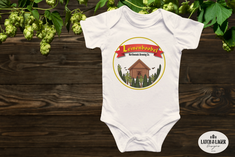 White baby onesie with a logo on a wooden surface with greenery