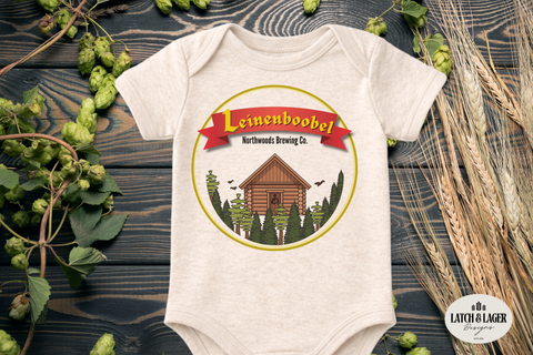 Baby onesie with 'Leinenboobel' branding on a wooden surface with hops and wheat.