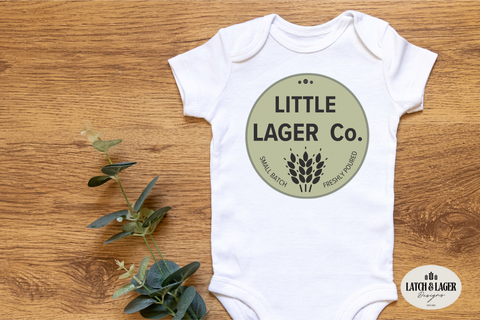 White baby onesie with 'Little Lager Co.' design on a wooden surface