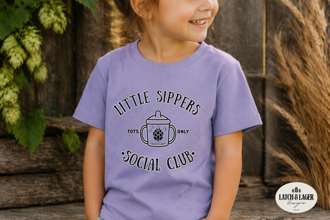 Child wearing a purple t-shirt with 'Little Sippers Social Club' text and graphic, standing outdoors.