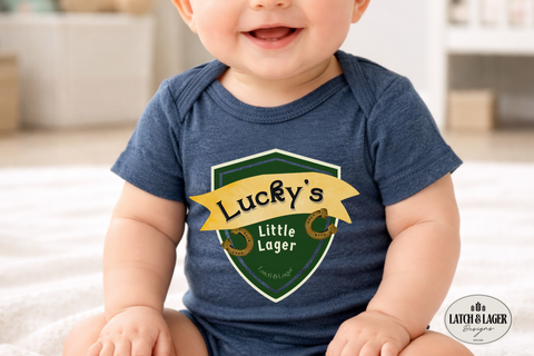 Baby wearing a blue onesie with 'Lucky's Little Lager' design, sitting on a carpeted floor.