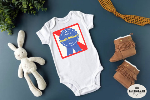 White baby onesie with a red and blue design, accompanied by a plush bunny and brown boots on a dark surface.