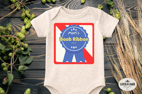 Beige baby onesie with 'Mom's Boob Ribbon' design on a wooden surface with greenery.