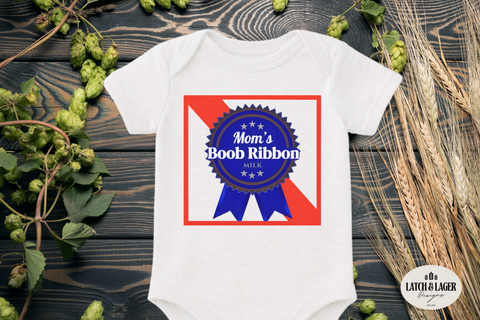 White baby onesie with 'Mom's Boob Ribbon' design on a wooden surface with plants.
