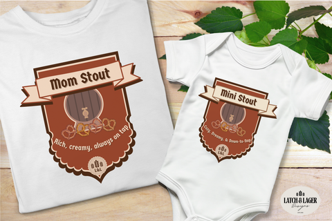 White t-shirt and baby onesie with 'Mom Stout' and 'Mini Stout' designs on a wooden surface with green leaves.