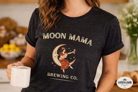 Person wearing a 'Moon Mama Brewing Co.' t-shirt holding a mug in a kitchen setting.