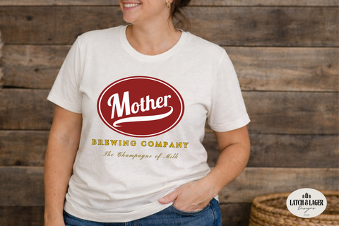Person wearing a white t-shirt with 'Mother Brewing Company' logo against a wooden background