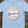 Light blue t-shirt with 'Sassyfras' logo on a wooden surface with hops and wheat.