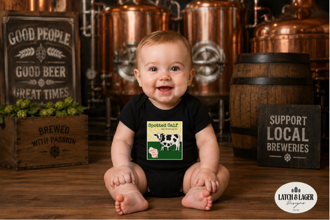 Baby wearing a black onesie with a cow graphic in a brewery setting