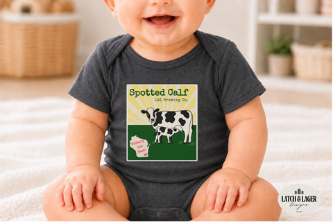 Baby wearing a dark gray onesie with a cow design and text, sitting on a light-colored surface.