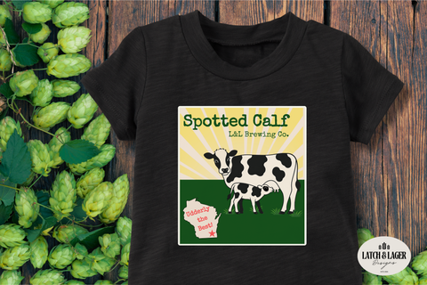 Black t-shirt with a cow graphic and text on a wooden surface with hops.