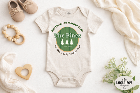 Baby onesie with 'The Pines' logo on a white surface with baby items.