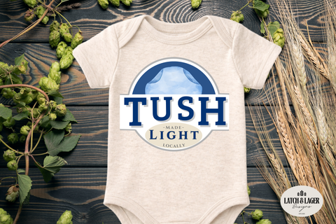 Beige baby onesie with 'TUSH Light' design on a wooden surface with plants.