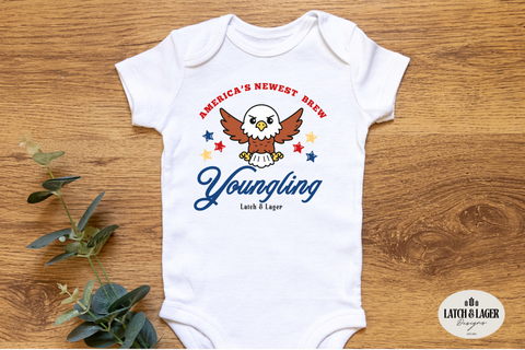 White baby onesie with an eagle design and text on a wooden surface