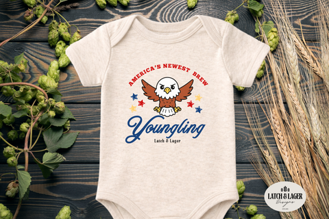 Baby onesie with 'Youngling' branding on a wooden surface with hops and barley.